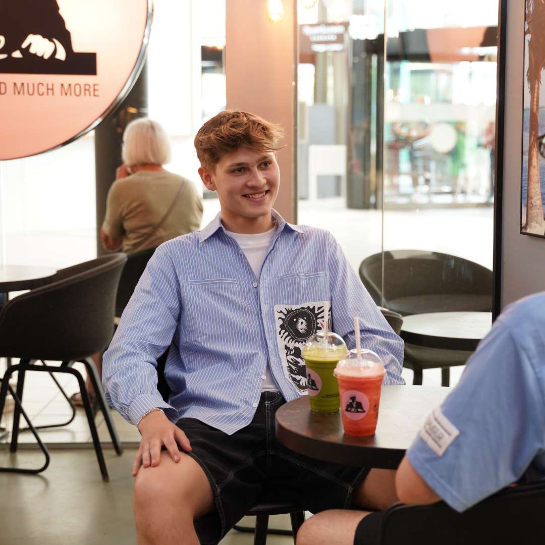 Smilende dreng sidder med en ven og drikker jucie fra Joe & the juice i Randers.